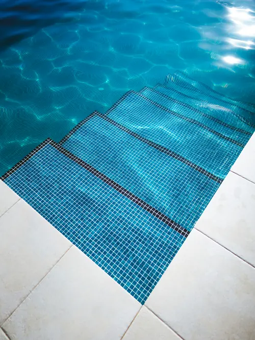Pool steps finished in blue glass mosaic tiles beside pale stone coping