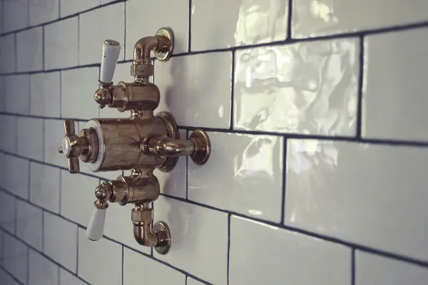Close-up of glossy white subway tiles around brass shower taps