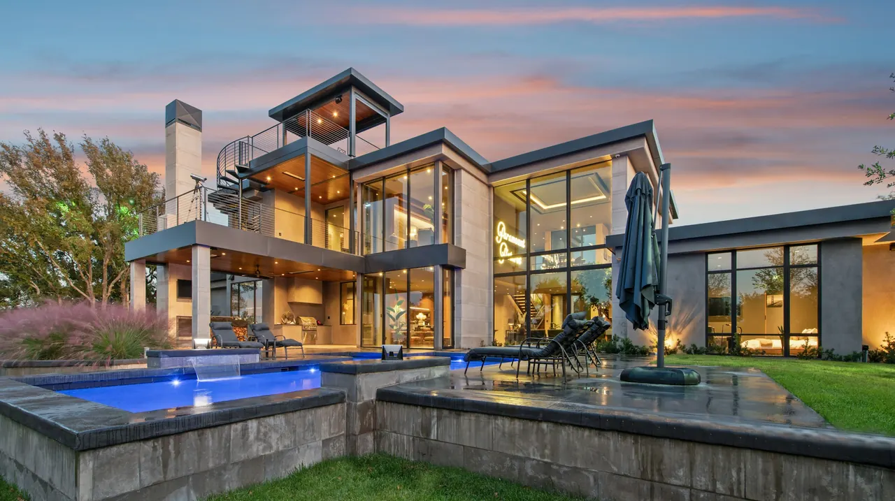 Contemporary home with glass walls and a lit pool at sunset