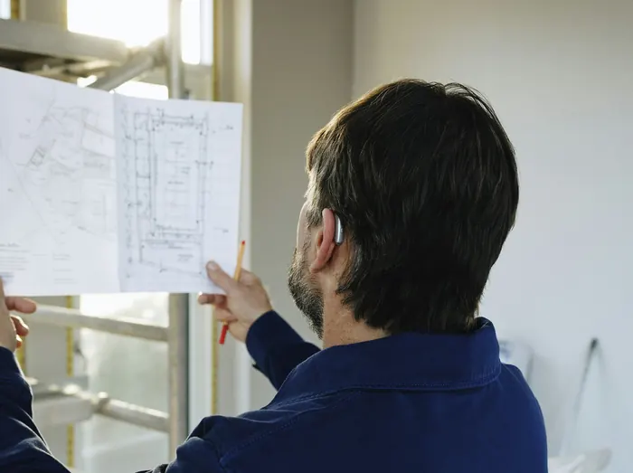 Builder holding up the plans in a room under renovation