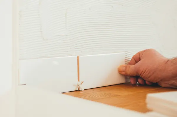 Tiler pressing a white wall tile into place against a levelling clip