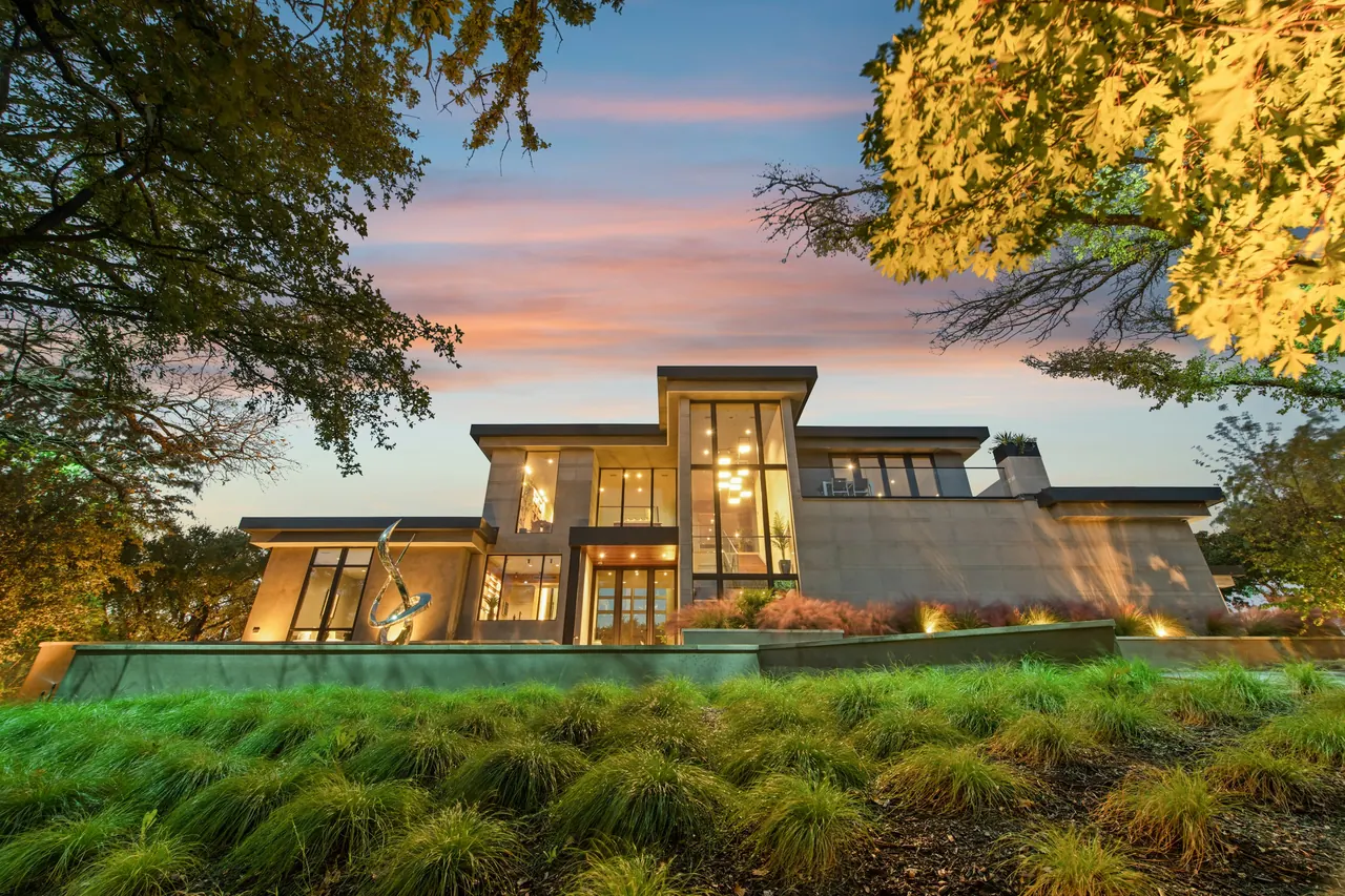 Contemporary home at dusk, its tall windows lit behind a garden of native grasses